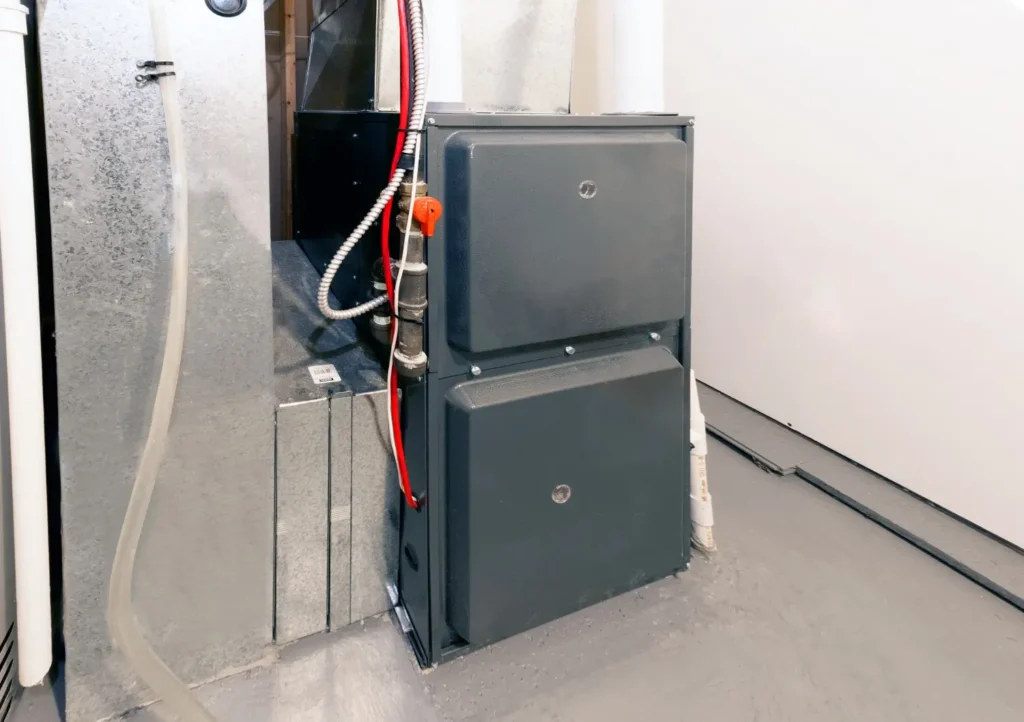 A newly installed gray furnace unit stands in a utility room next to galvanized ductwork.